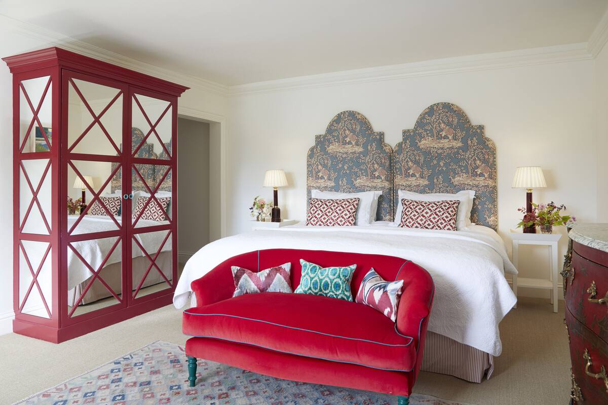 A bedroom with a red upholstered sofa, a large bed with patterned headboard, and a red wardrobe.