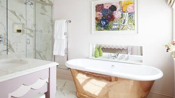 Un bagno con doccia in marmo, lavabo bianco, vasca da bagno in rame e un'opera d'arte colorata appesa al muro.