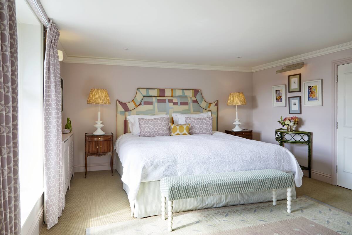 A bedroom with a large bed, two bedside tables, a bench, and a wall with framed pictures.