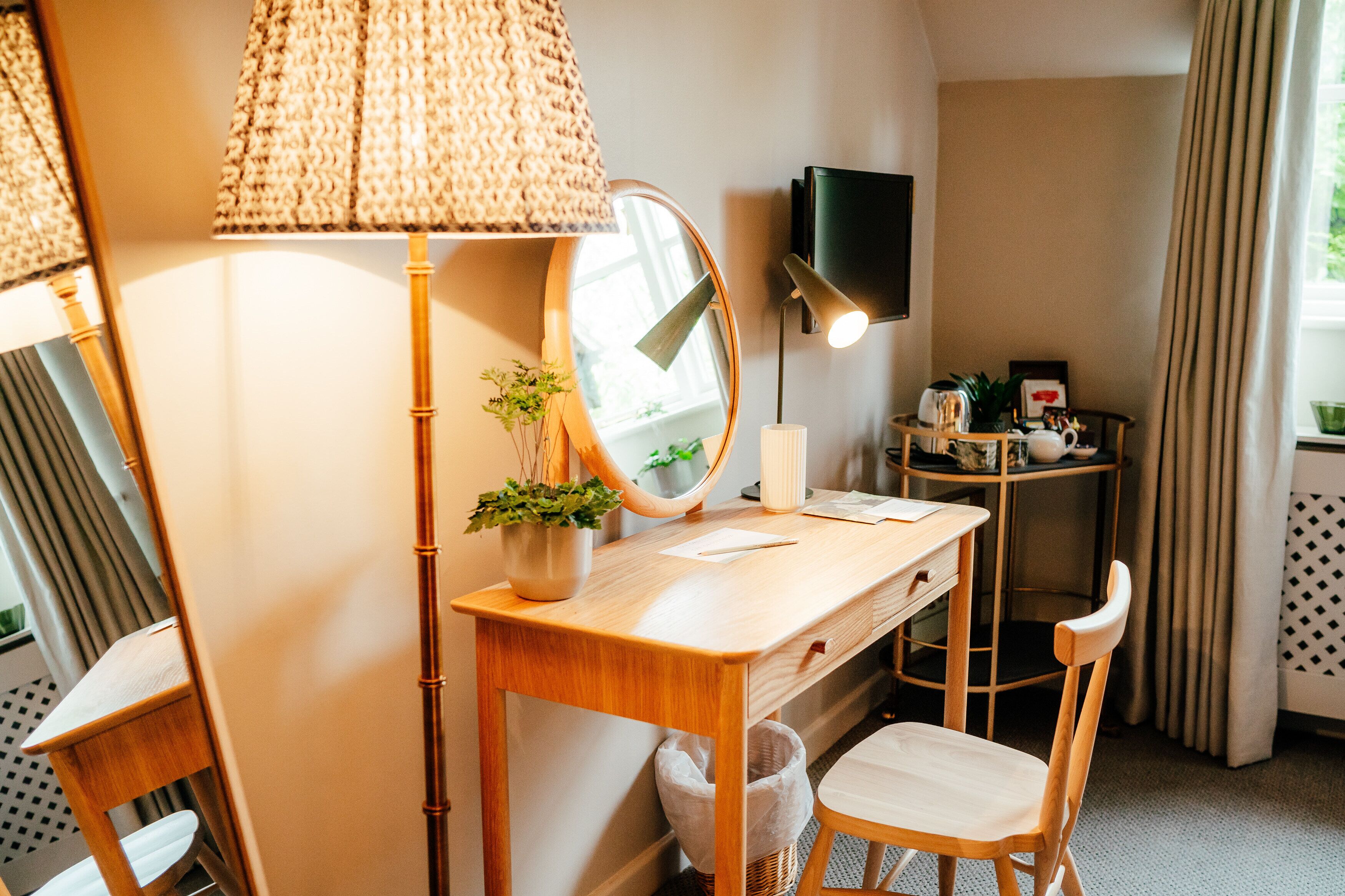 A wooden desk with a mirror, a lamp, a small potted plant, and a chair.