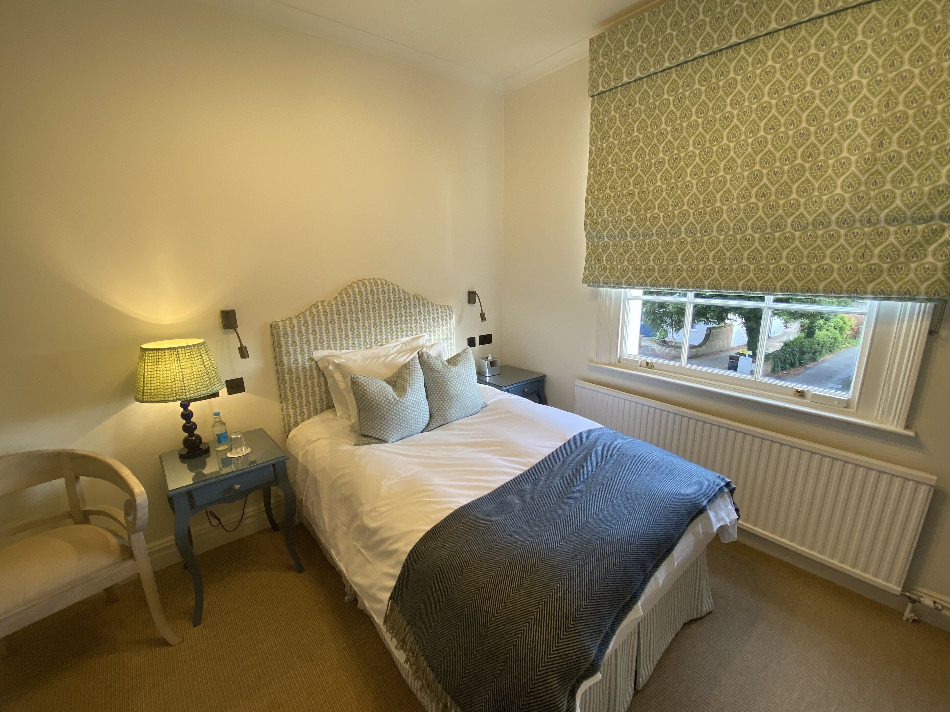 Un dormitorio con cama, mesita de noche, lámpara, silla y ventana con vistas.
