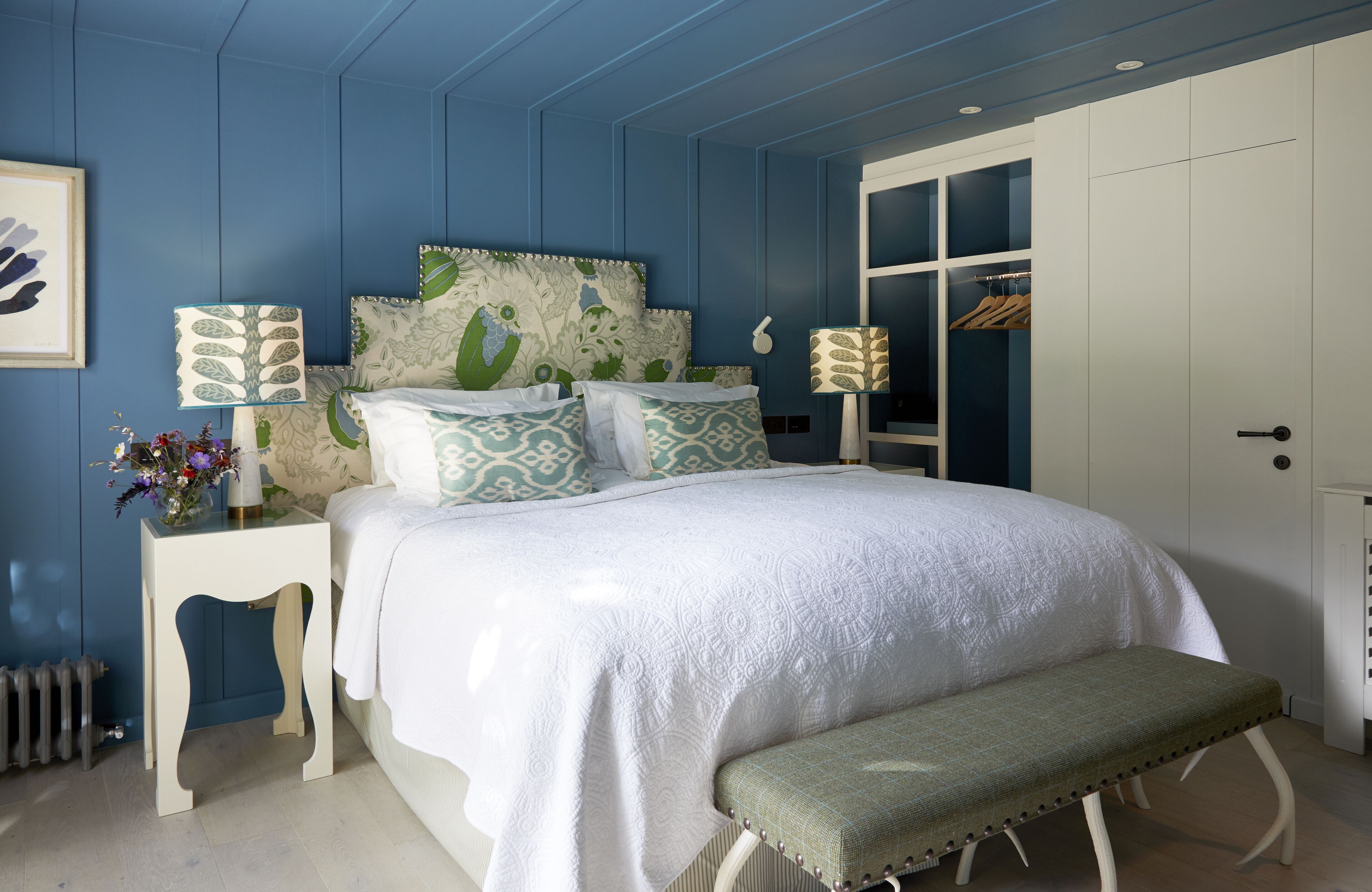 A bedroom with a bed, bedside tables, a bench, a wardrobe, and a radiator.