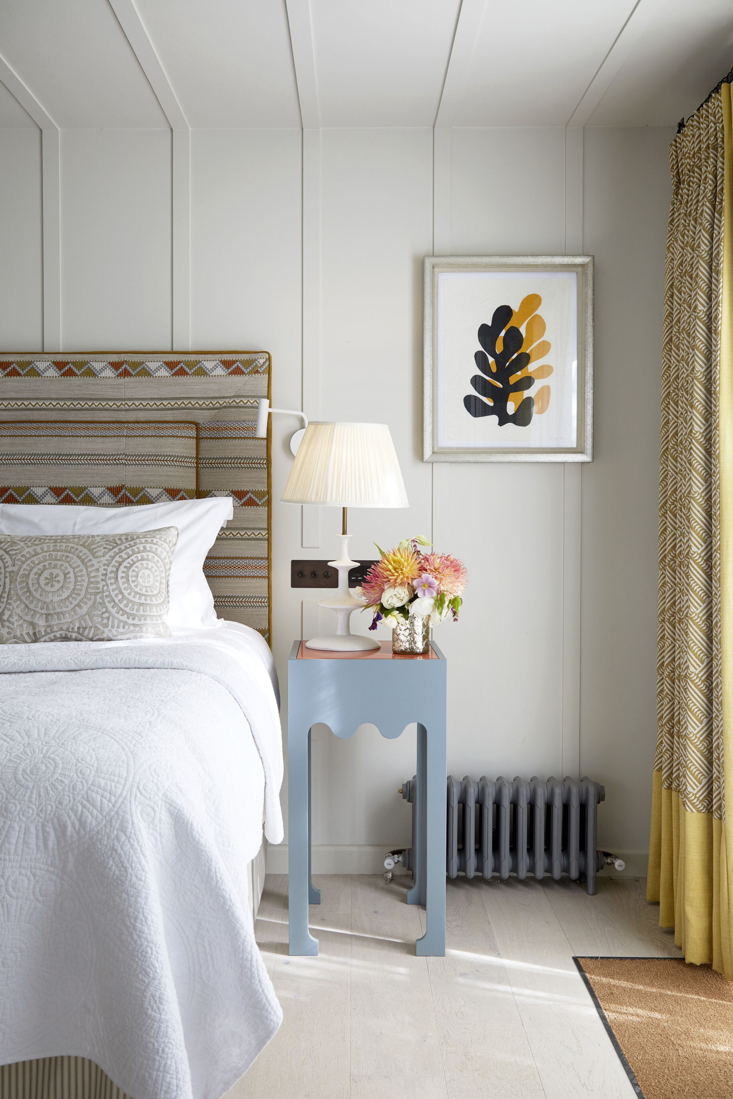 A neatly arranged bedroom with a bed, bedside table, lamp, and a framed artwork on the wall.