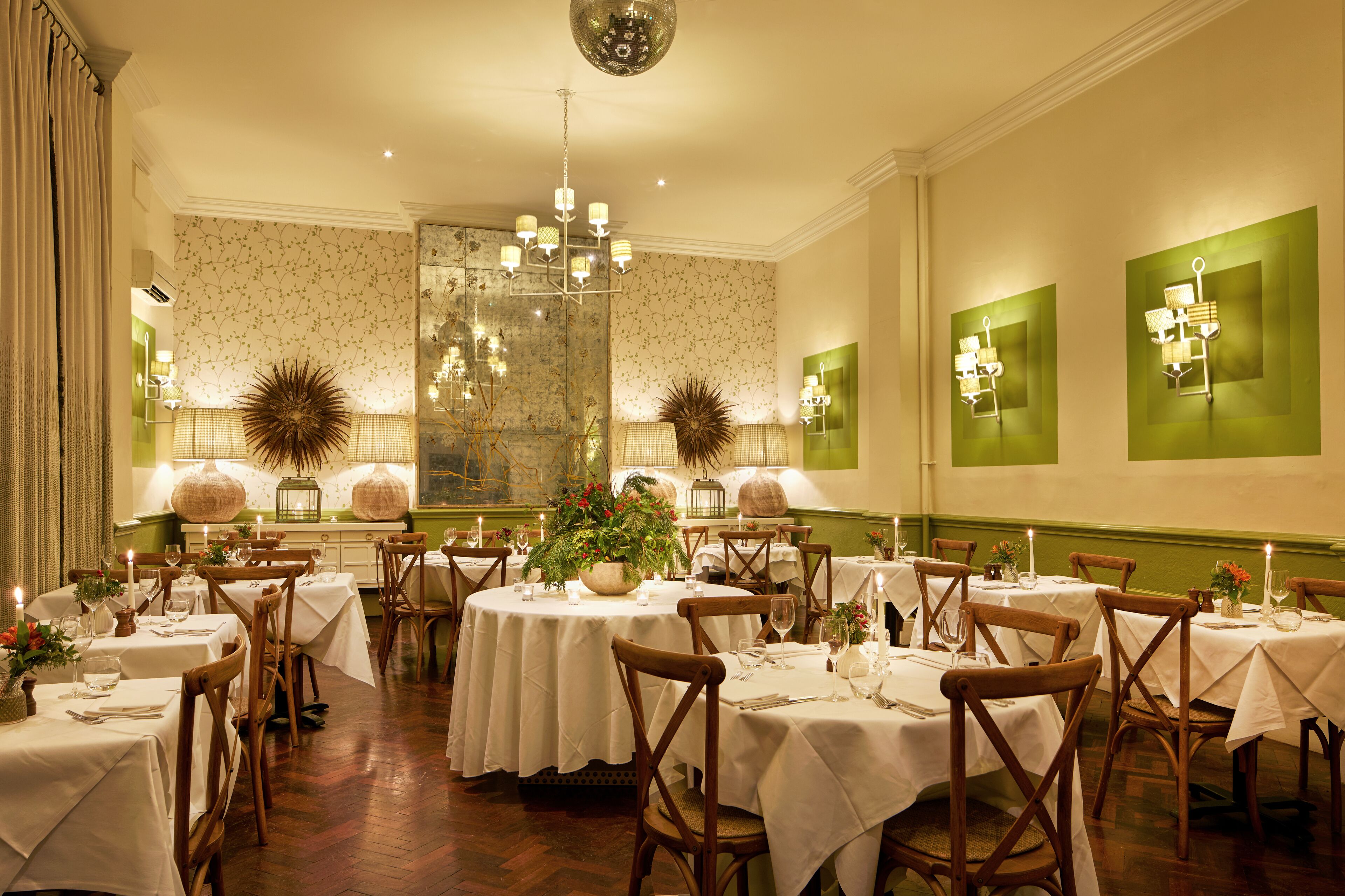 Comedor formal con mesas redondas, sillas de madera y apliques en la pared verde.
