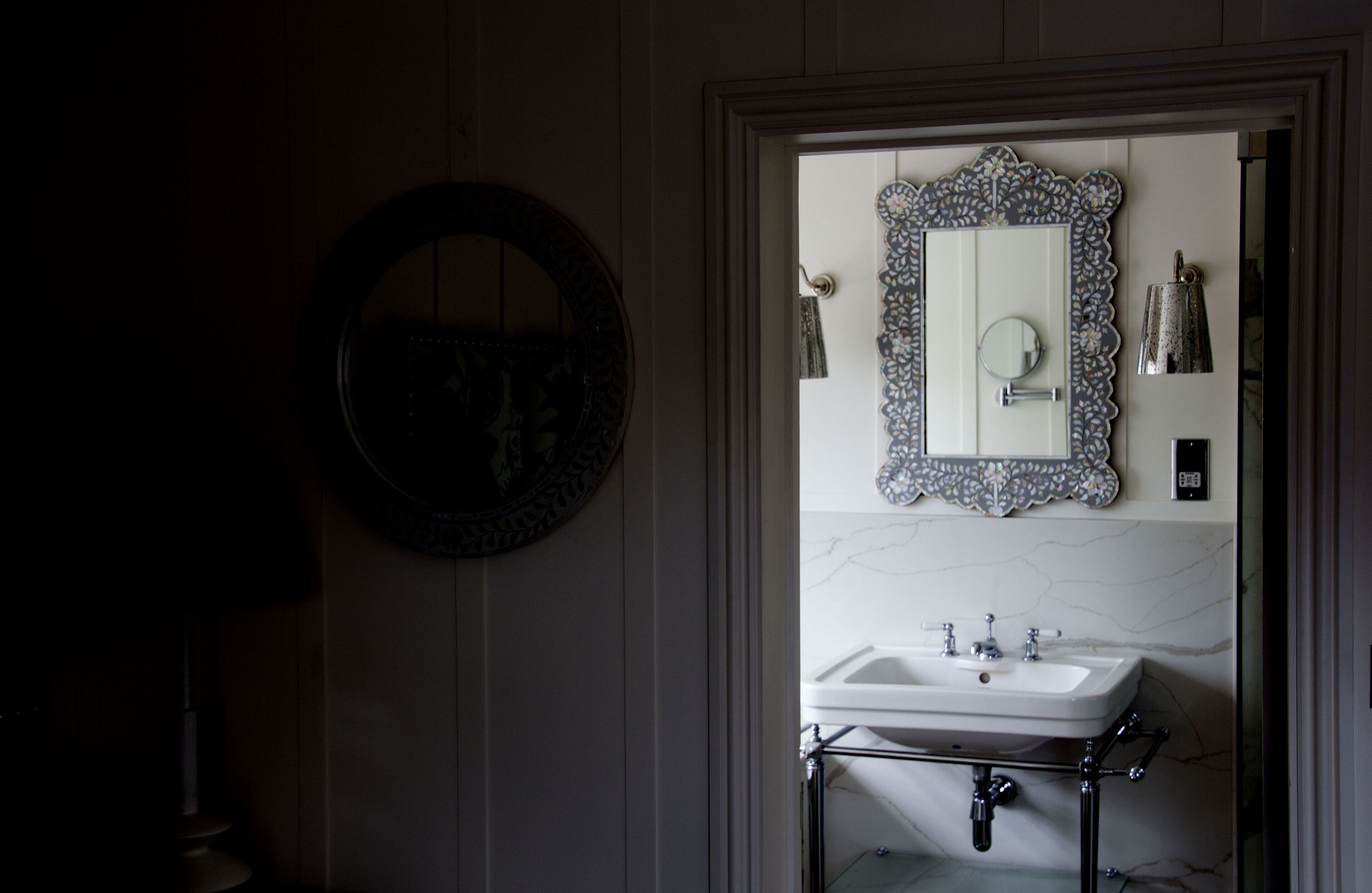 Een badkamer met een ronde spiegel, een rechthoekige spiegel en een witte wastafel met chroombeslag.