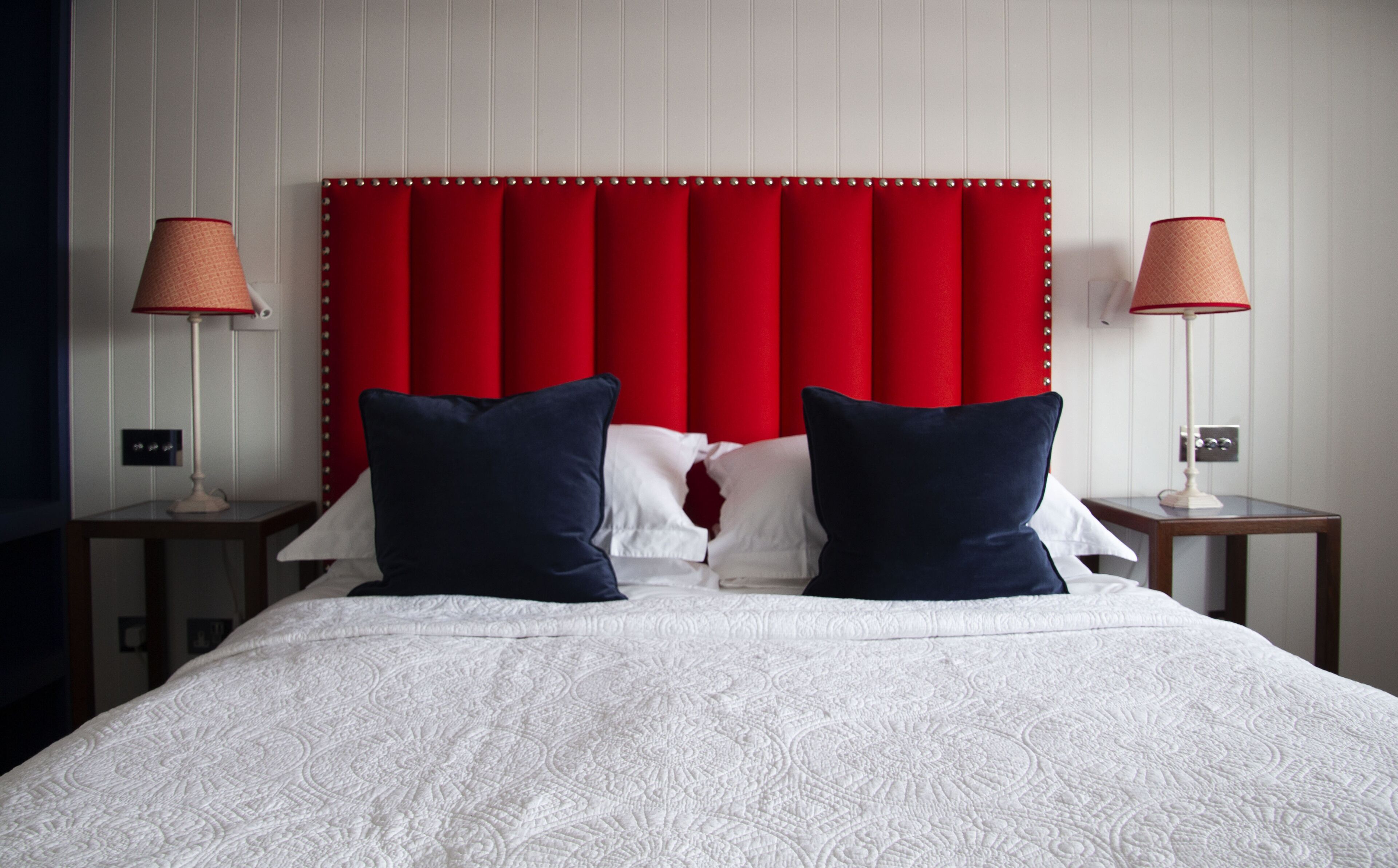 A hotel room with a red upholstered headboard, two bedside lamps, and a white bedspread.