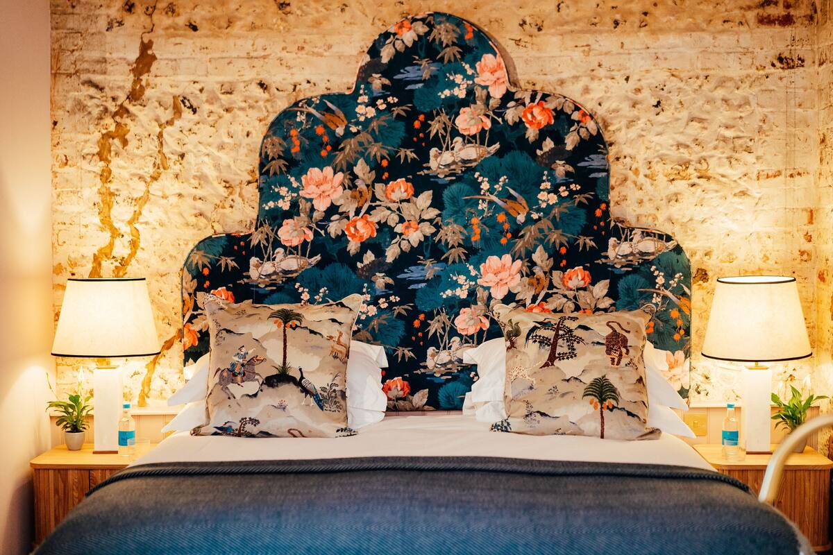 A bed with floral-patterned pillows and a headboard against a textured wall.