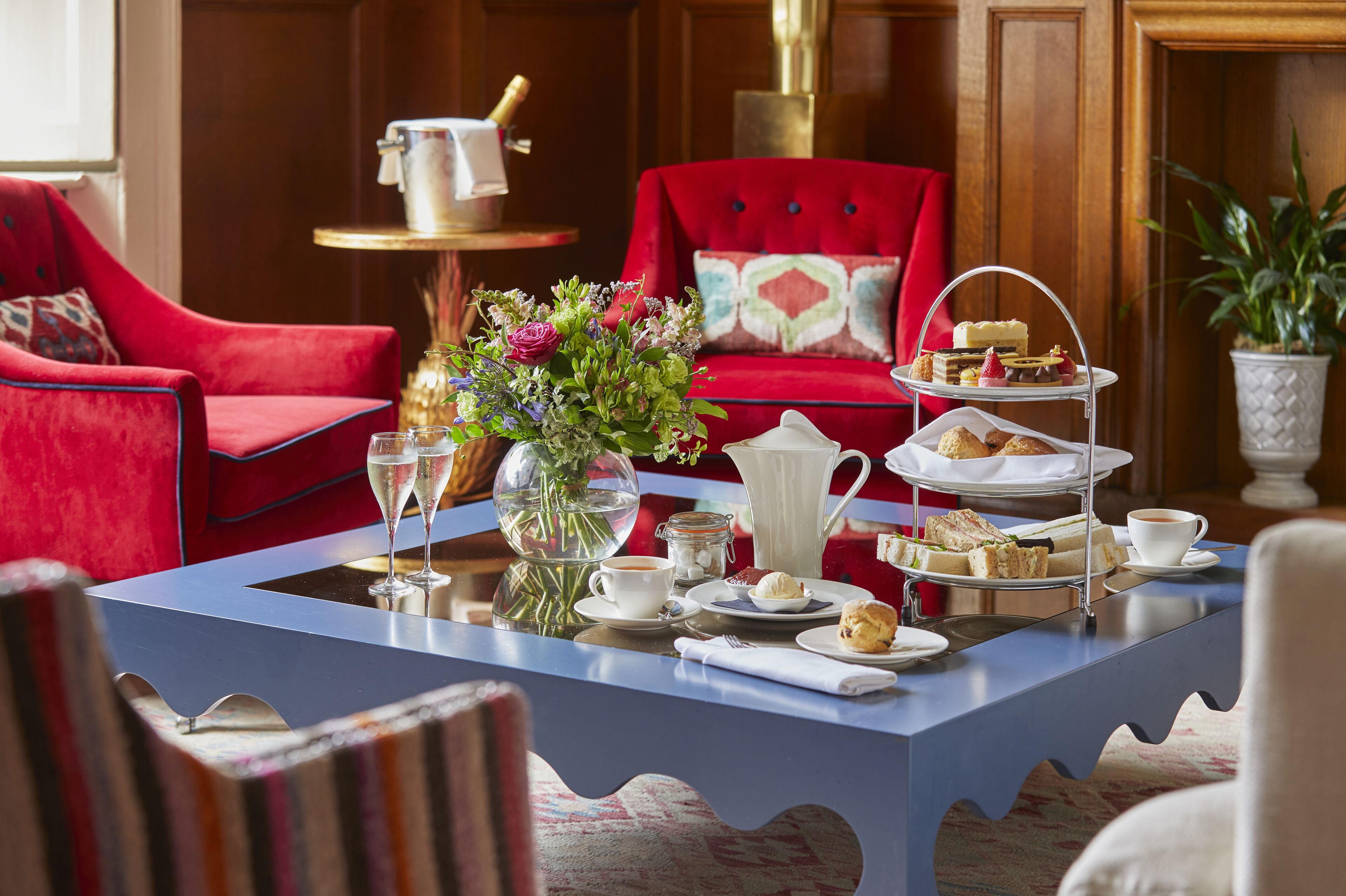 A room with a red armchair, a blue table with a tea set, and a vase with flowers.