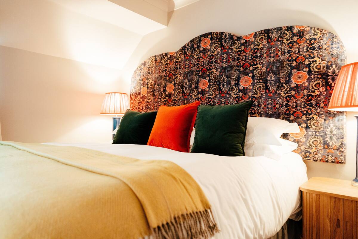 A neatly made bed with a patterned headboard, two bedside lamps, and a bedside table.
