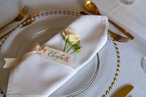 A table setting with a white napkin, a name tag, a white rose, and gold cutlery. - The Grosvenor Stockbridge (Stockbridge)