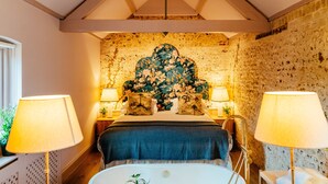 Une chambre à coucher avec un grand lit, deux lampes de chevet, une tête de lit en bois, une baignoire et une petite table sur laquelle est posée une plante.
