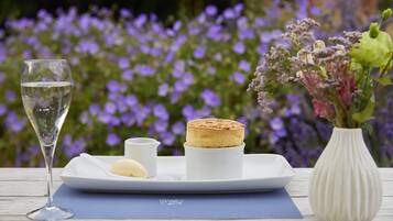 A table setting with a glass of water, a small white dish, a white plate with a cake, and a vase with flowers.
