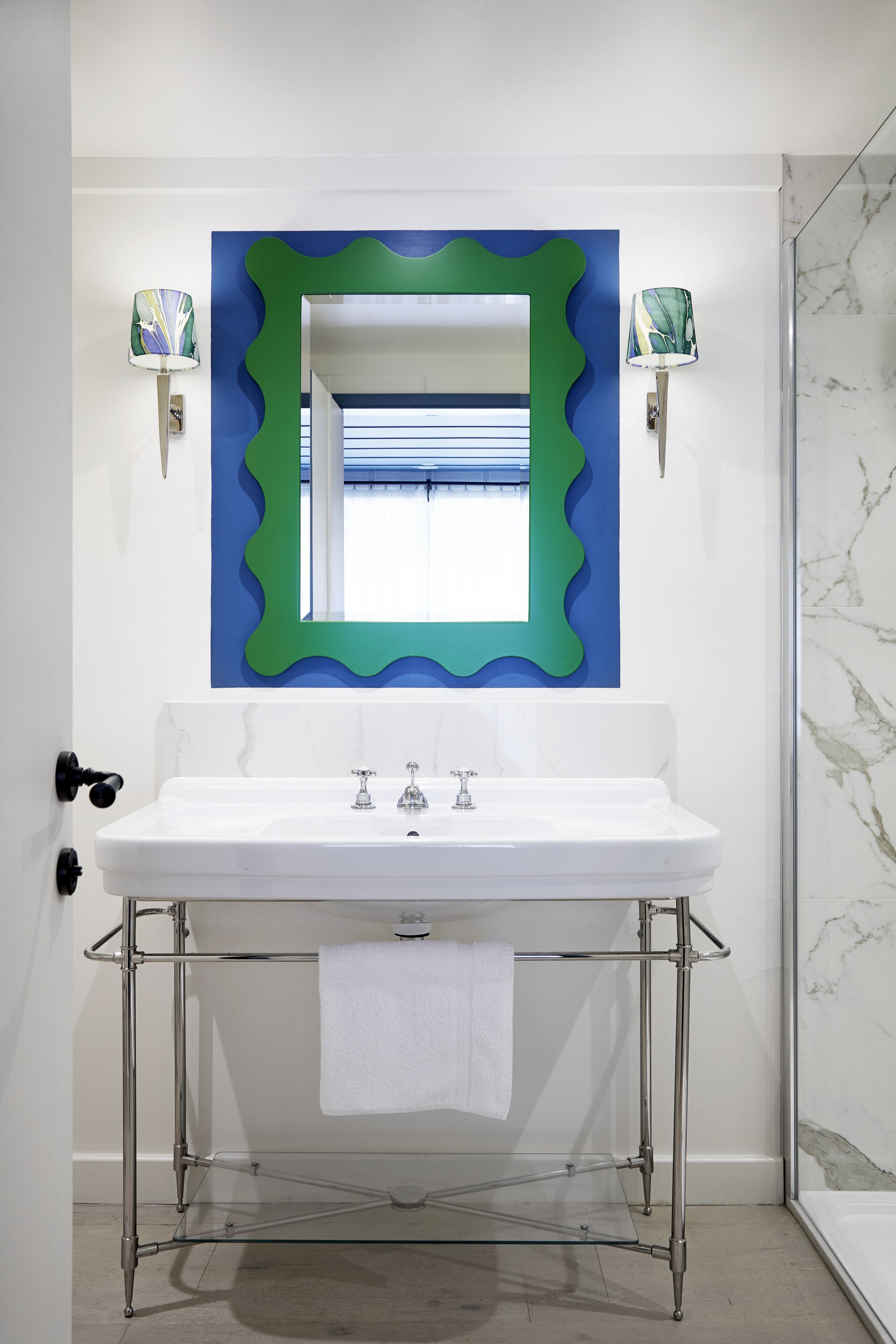 A bathroom with a white sink, a green-framed mirror, and a glass shelf below.