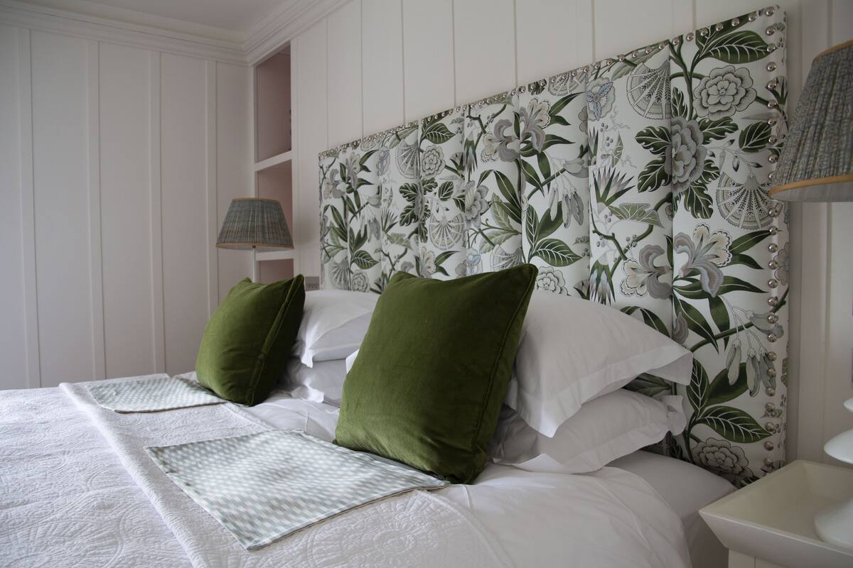 A neatly made bed with green and white pillows, a patterned headboard, and a bedside lamp.