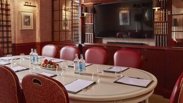 A formal meeting room with a round table, leather chairs, a large flat-screen TV, and bookshelves.