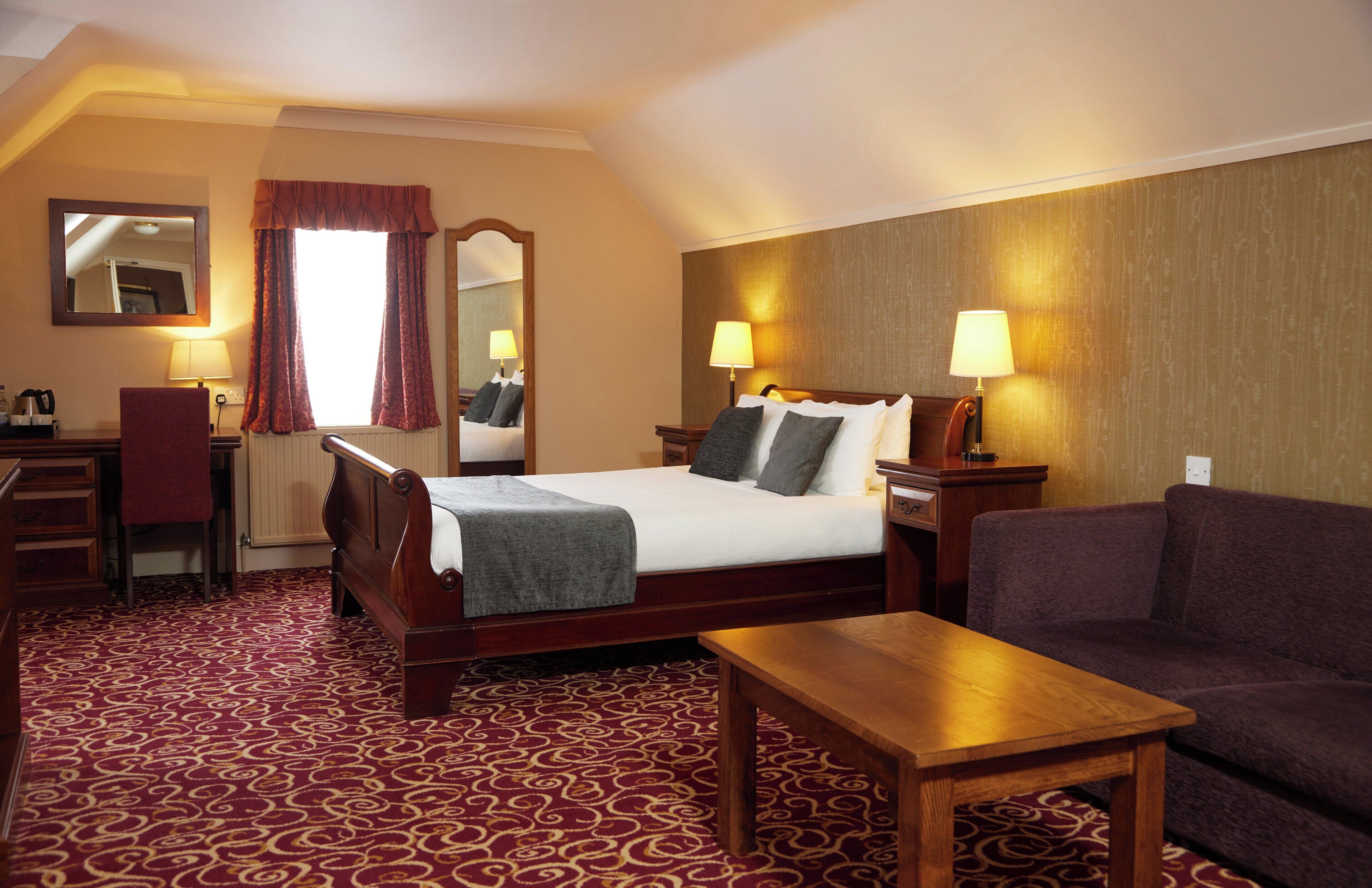 Habitación de hotel con cama, dos lámparas de noche, una mesa de madera, un sofá, un escritorio con una silla y un espejo.