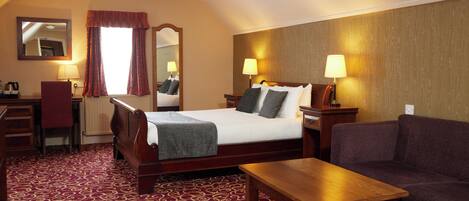 Habitación de hotel con cama, dos lámparas de noche, una mesa de madera, un sofá, un escritorio con una silla y un espejo.
