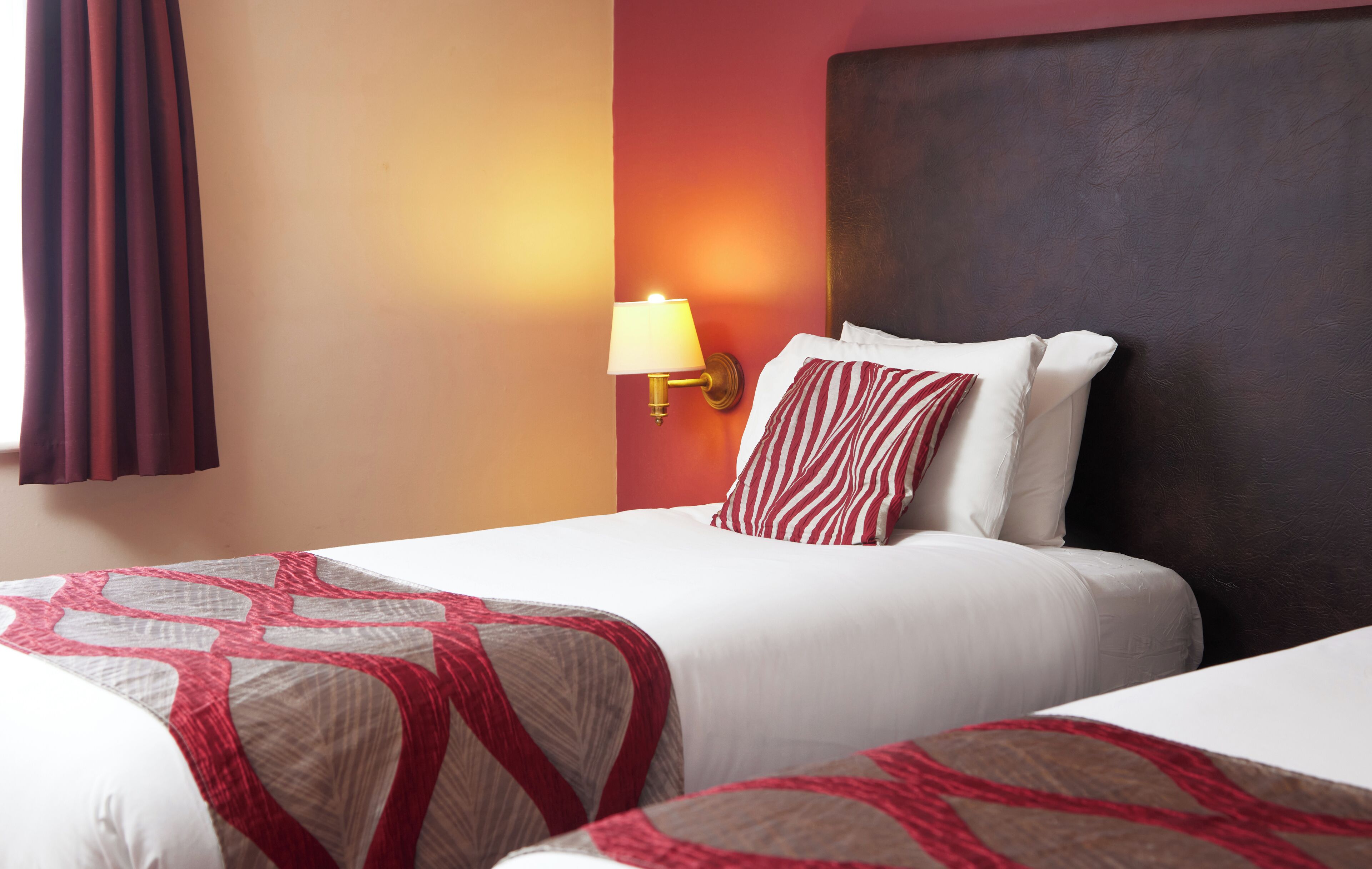 Habitación de hotel con dos camas, una lámpara de pared y una ventana con cortinas.