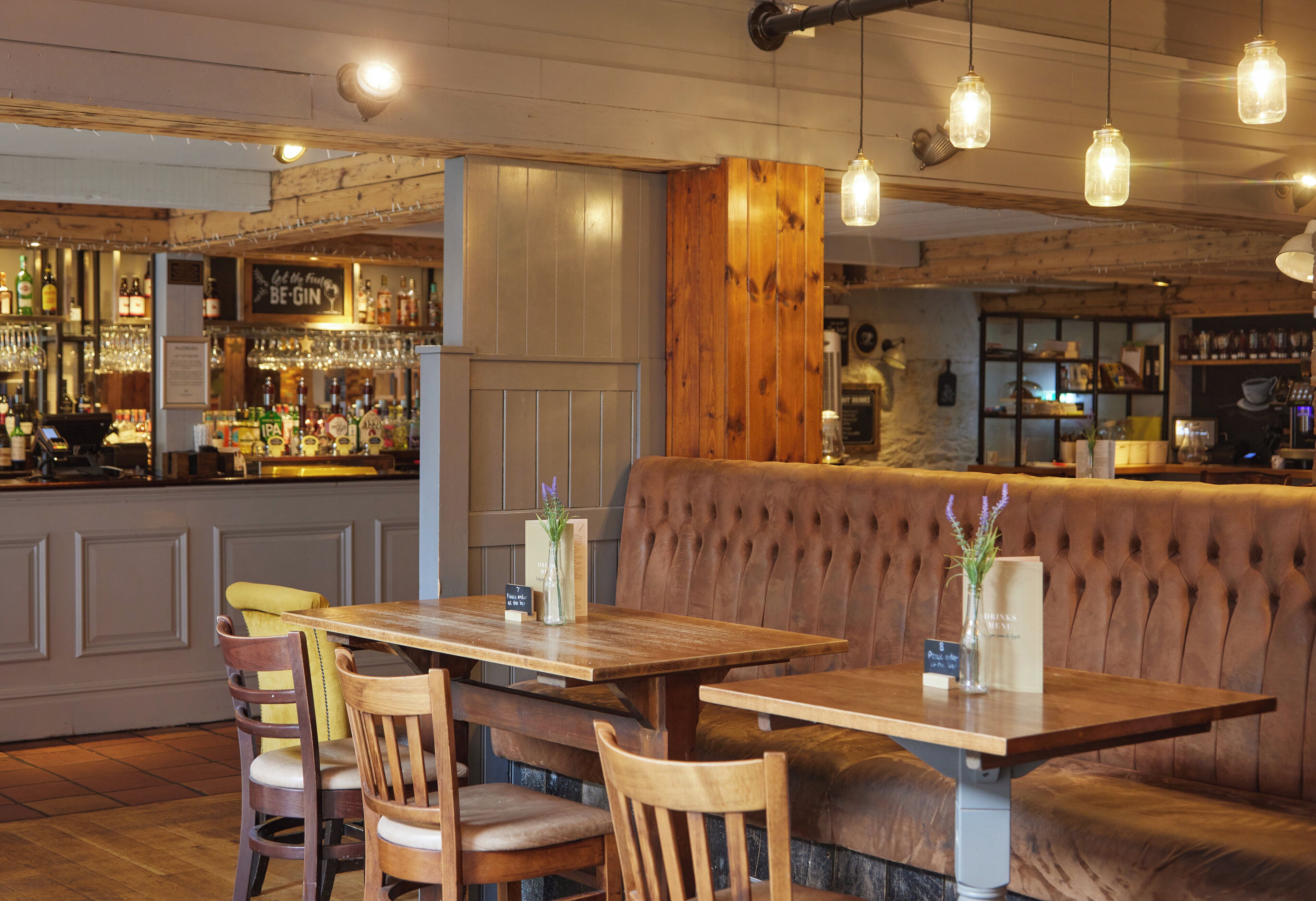 A restaurant with wooden tables and chairs, a bar area, and a seating area with a cushioned bench.