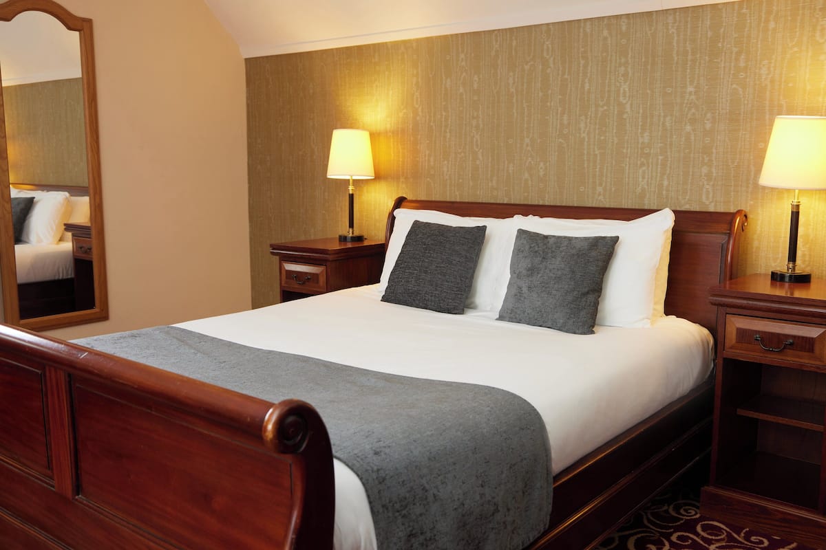A neatly made bed with a wooden headboard, two bedside tables with lamps, and a large mirror on the left.