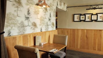 Una mesa de comedor de madera con una silla, un atril para menús y una pared decorada con cuadros.
