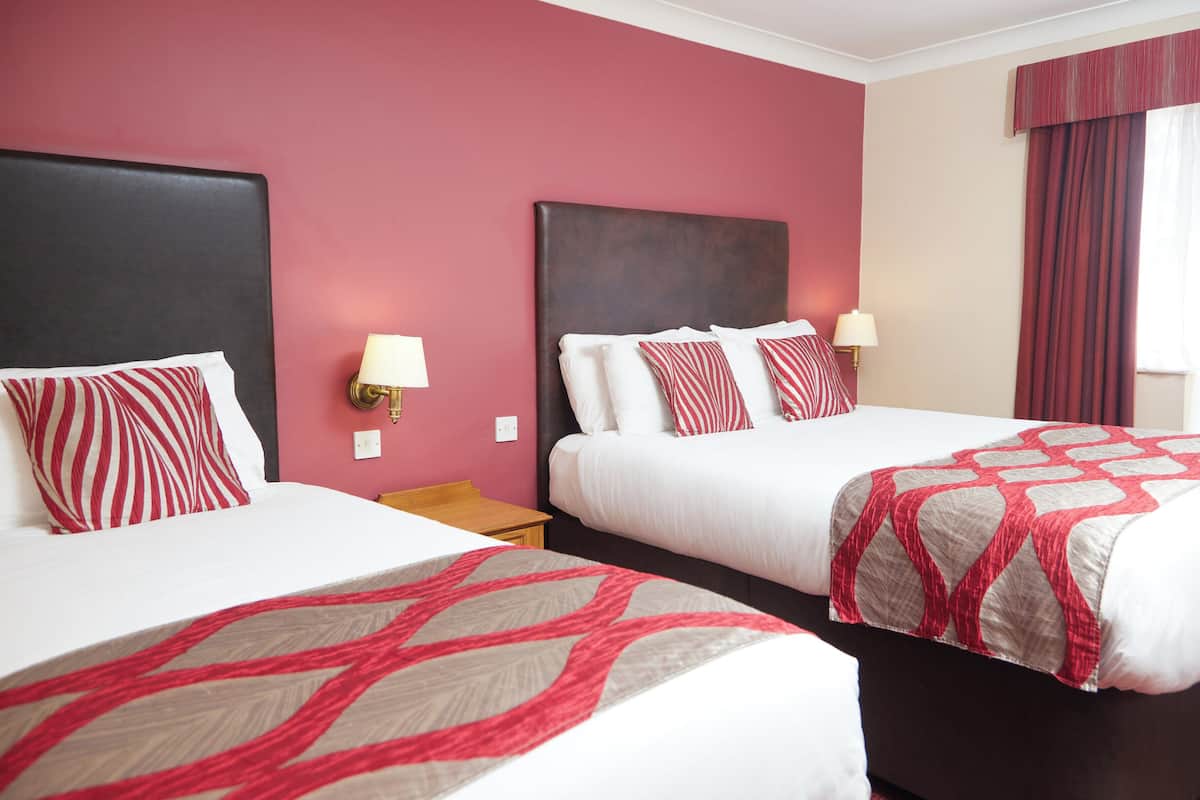A hotel room with two beds, each with white bedding and red-striped pillows. There are wall-mounted lamps on either side of the beds.