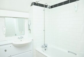Casa de banho com lavatório branco, espelho e área de chuveiro com banheira branca.