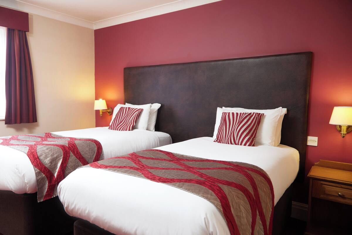 A hotel room with two beds, each with a red and white patterned bedspread, a dark headboard, and bedside lamps.