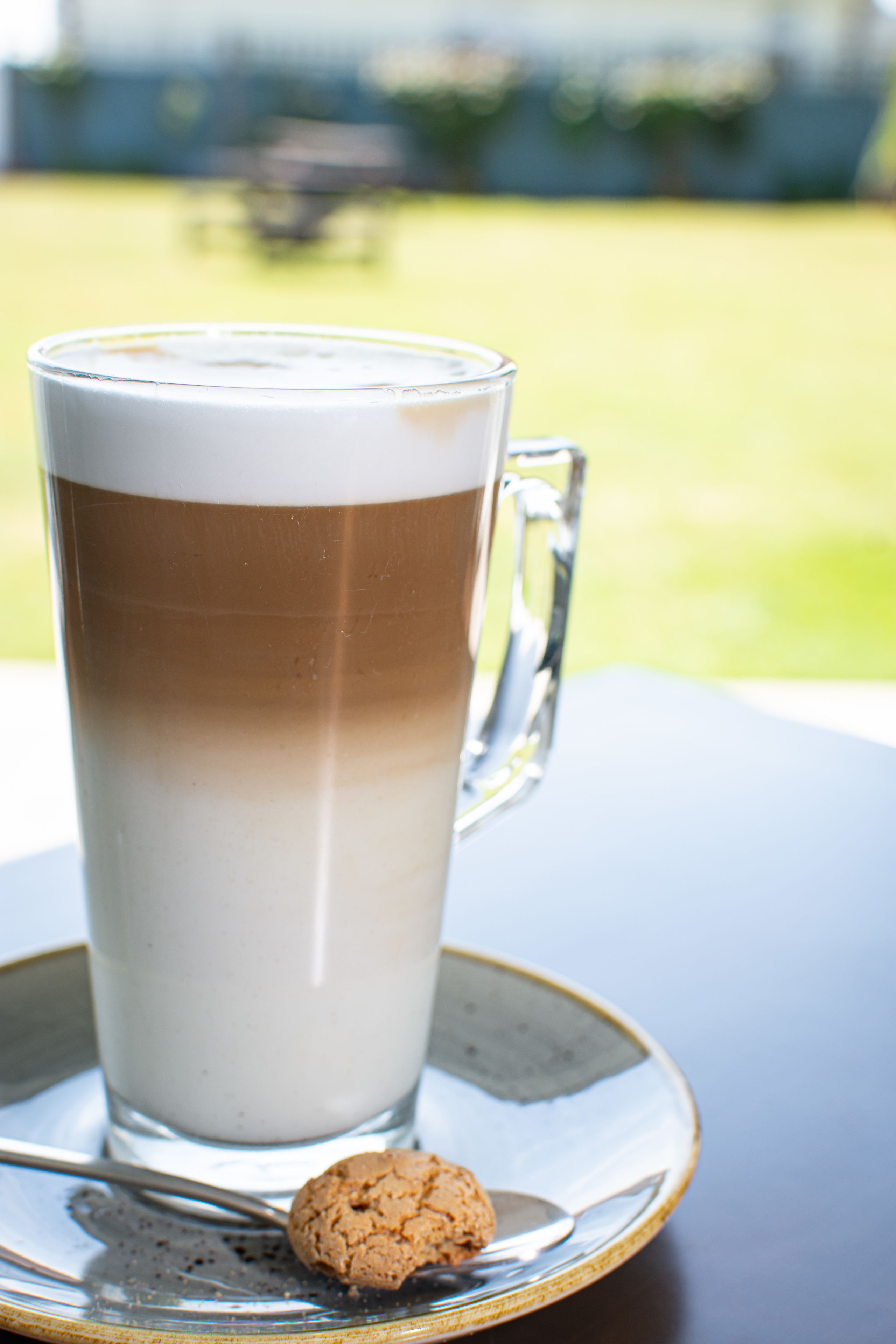 Un'alta tazza di vetro con una bevanda a strati, un biscotto e un cucchiaio su un piattino.