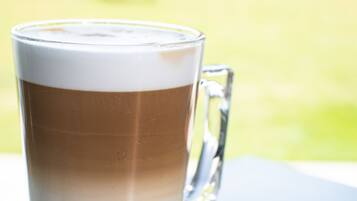 Un'alta tazza di vetro con una bevanda a strati, un biscotto e un cucchiaio su un piattino.