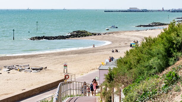 A coastal beach scene with a clear walkway leading to the shore, a pier in the distance, and a few boats on the water. - Kingscliff Hotel (Clacton-on-Sea)