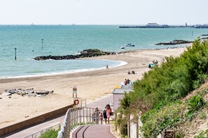 A coastal beach scene with a clear walkway leading to the shore, a pier in the distance, and a few boats on the water. - Kingscliff Hotel (Clacton-on-Sea)