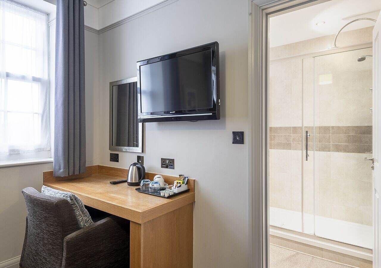 Ein Hotelzimmer mit Holzschreibtisch, Flachbildfernseher, Kaffeemaschine und Duschbereich.