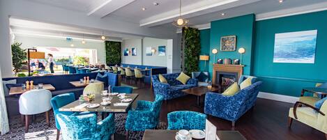 Un restaurante con sillas y mesas tapizadas en azul, paredes color verde azulado y una chimenea.