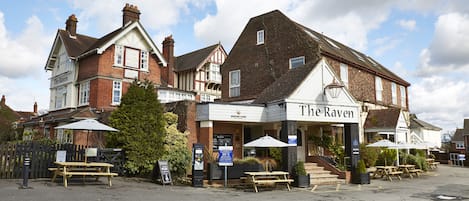 Un pub traditionnel appelé « The Raven », doté d’une terrasse et d’une façade en briques.