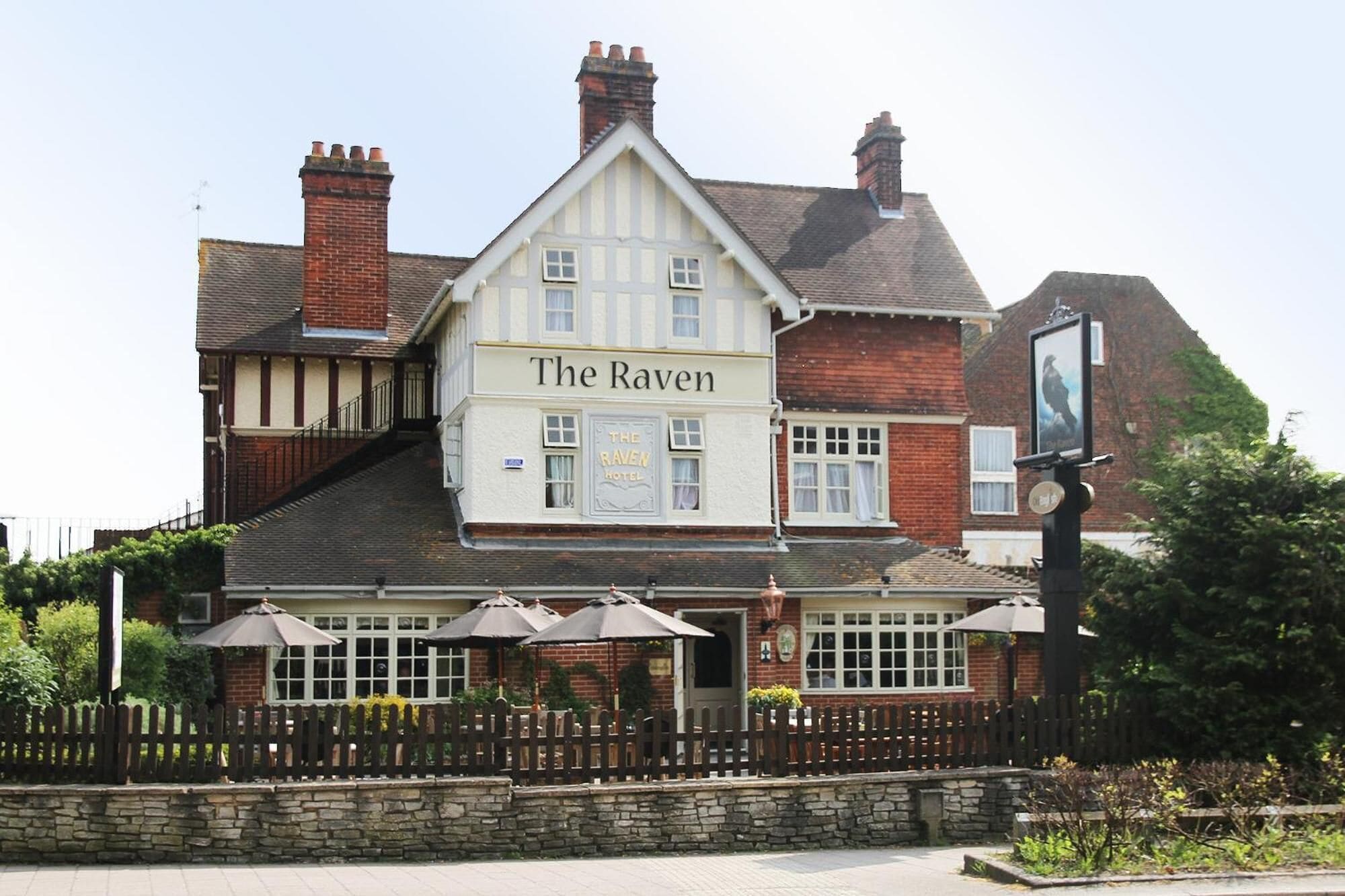 A traditional pub named "The Raven" with a white facade, multiple chimneys, and a stone wall in front.
