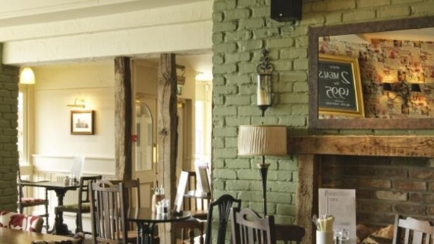 A dining area with brick walls, a fireplace, and a menu board. - The Raven Hotel by Greene King Inns (Hook)