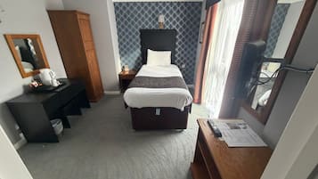 A hotel room with a bed, a desk, a wardrobe, a mirror, and a window with curtains.