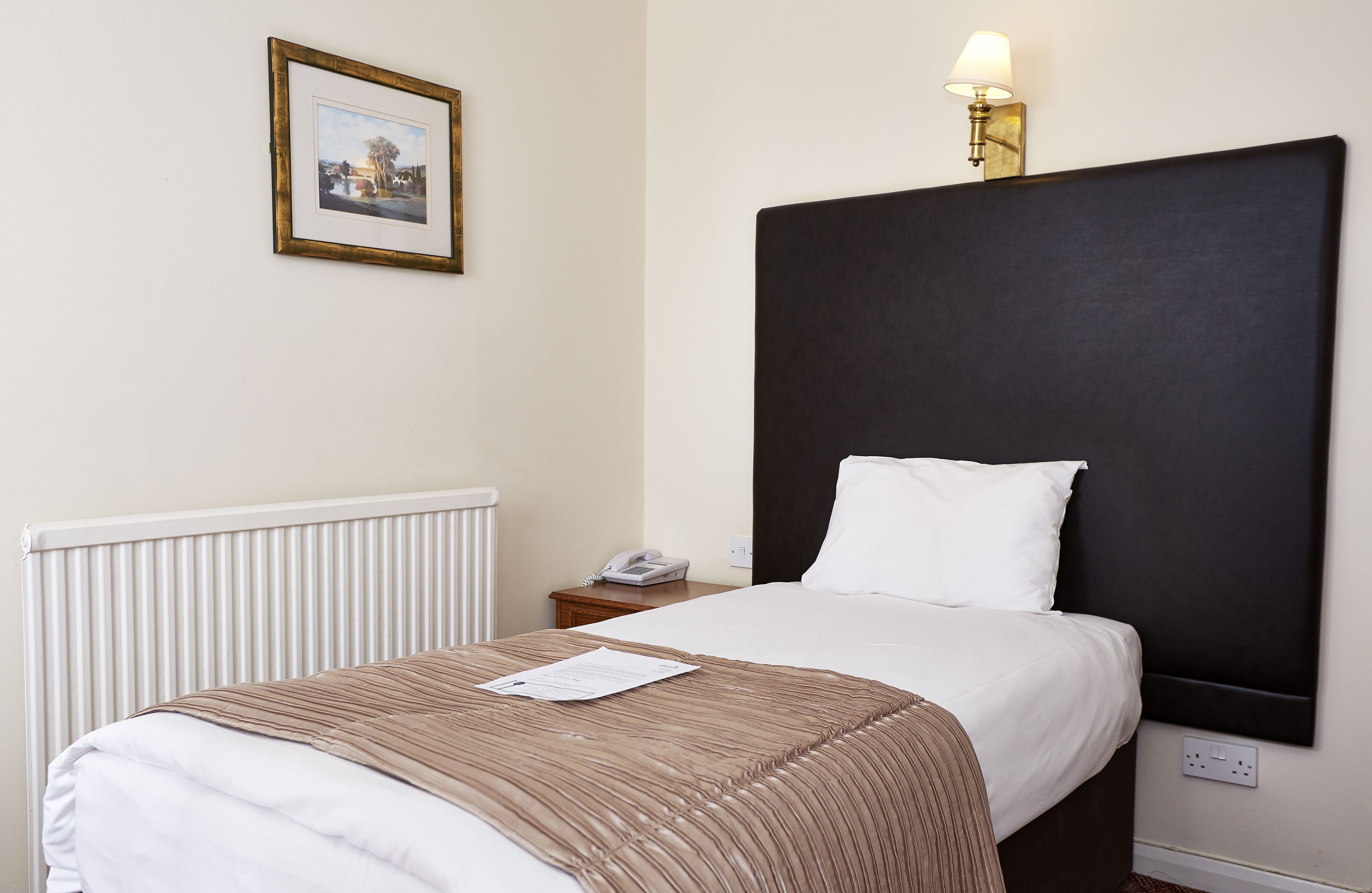 Habitación de hotel con una cama grande, una mesita de noche con lámpara, un cuadro en la pared y un radiador.