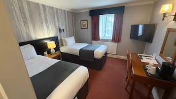 A hotel room with two beds, a desk with a chair, a TV, and a window with curtains.