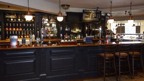 A bar area with a variety of liquor bottles, a selection of beers, and a menu board. - The Raven Hotel by Greene King Inns (Hook)