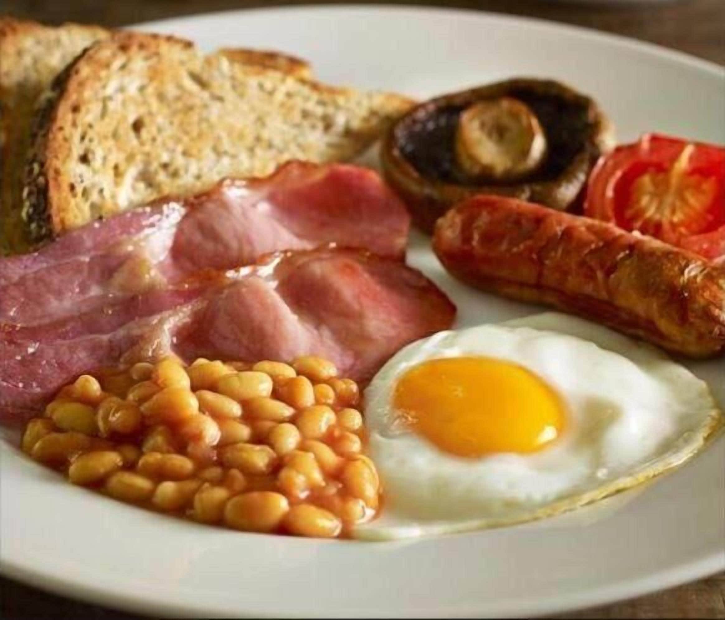 A plate of breakfast food including eggs, beans, bacon, sausages, mushrooms, and toast.