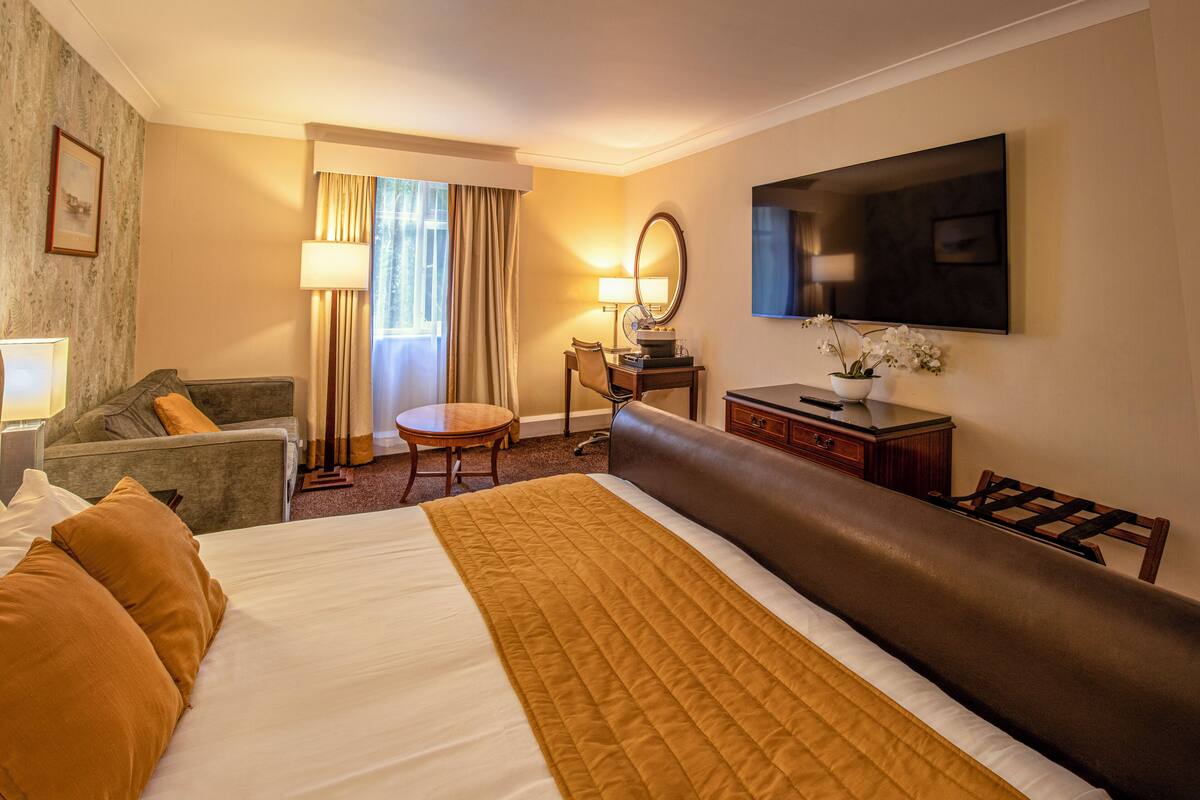 Ein Hotelzimmer mit einem großen Bett, einem Sofa, einem Schreibtisch, einem Fernseher und einem Fenster mit Vorhängen.