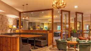A cozy restaurant with wooden decor, a seating area with a table and chairs, and a large mirror reflecting the interior. - Hollins Hall Hotel, Spa & Golf (Shipley)