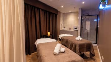 Relax in a serene spa room with two massage tables, a glass shower, and a wall-mounted sink.