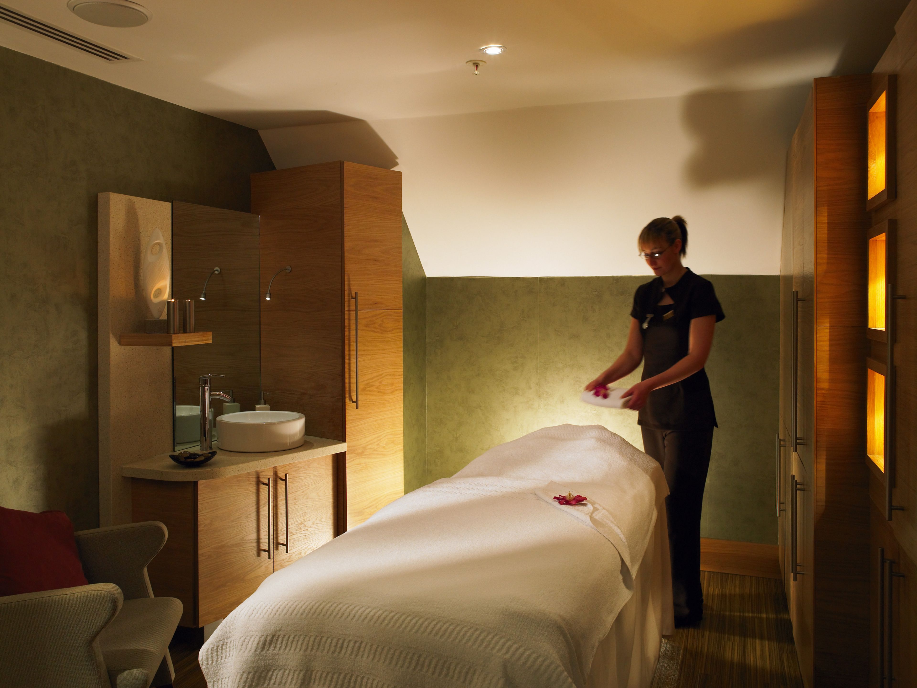 Un moderno cuarto de spa con una camilla de masaje, armarios de madera y un espejo grande.