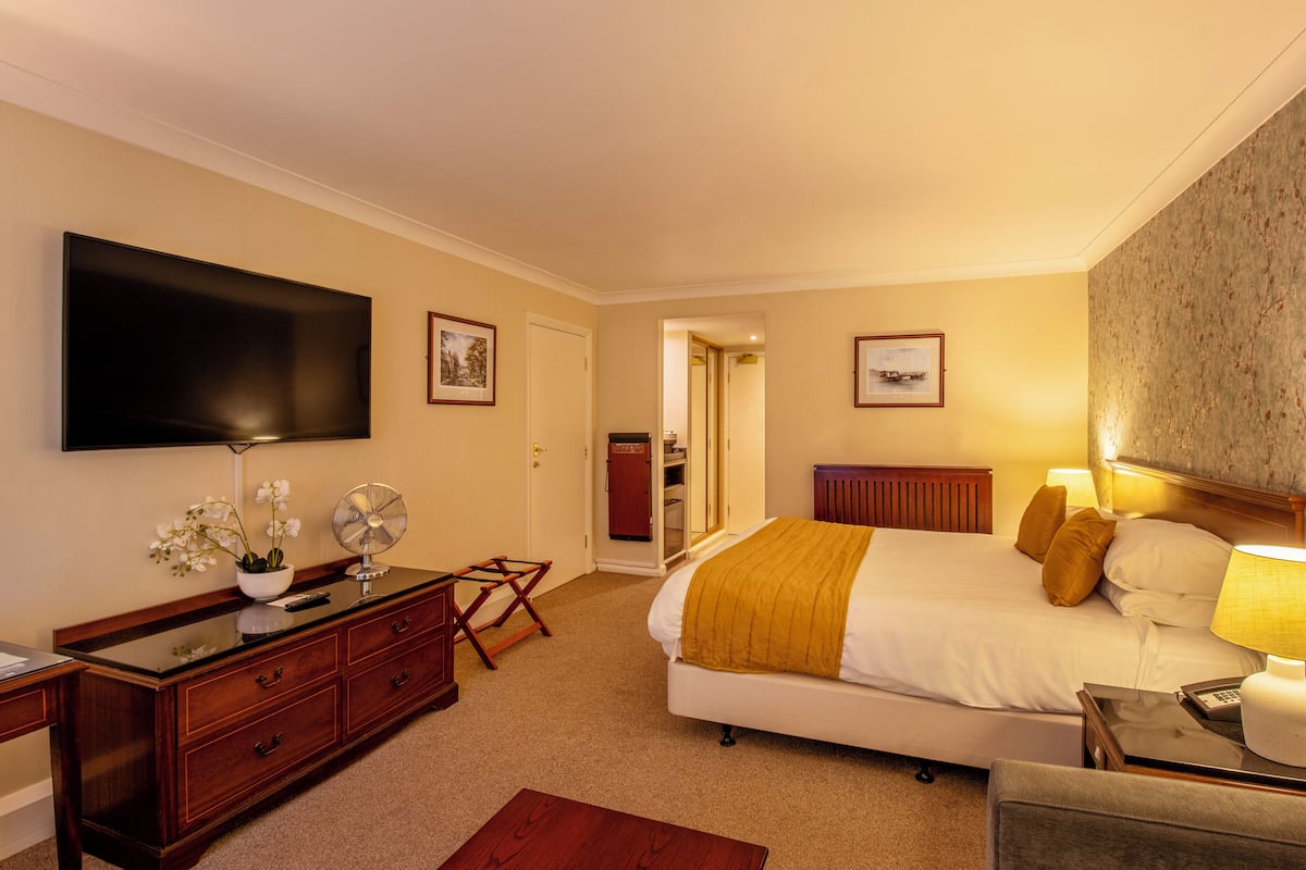 Ein Hotelzimmer mit Bett, Nachttisch, Lampe, Kommode, Fernseher und einer Tür zu einem Badezimmer.