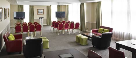 A hotel room with a conference area, red and green chairs, a sofa, and a TV.