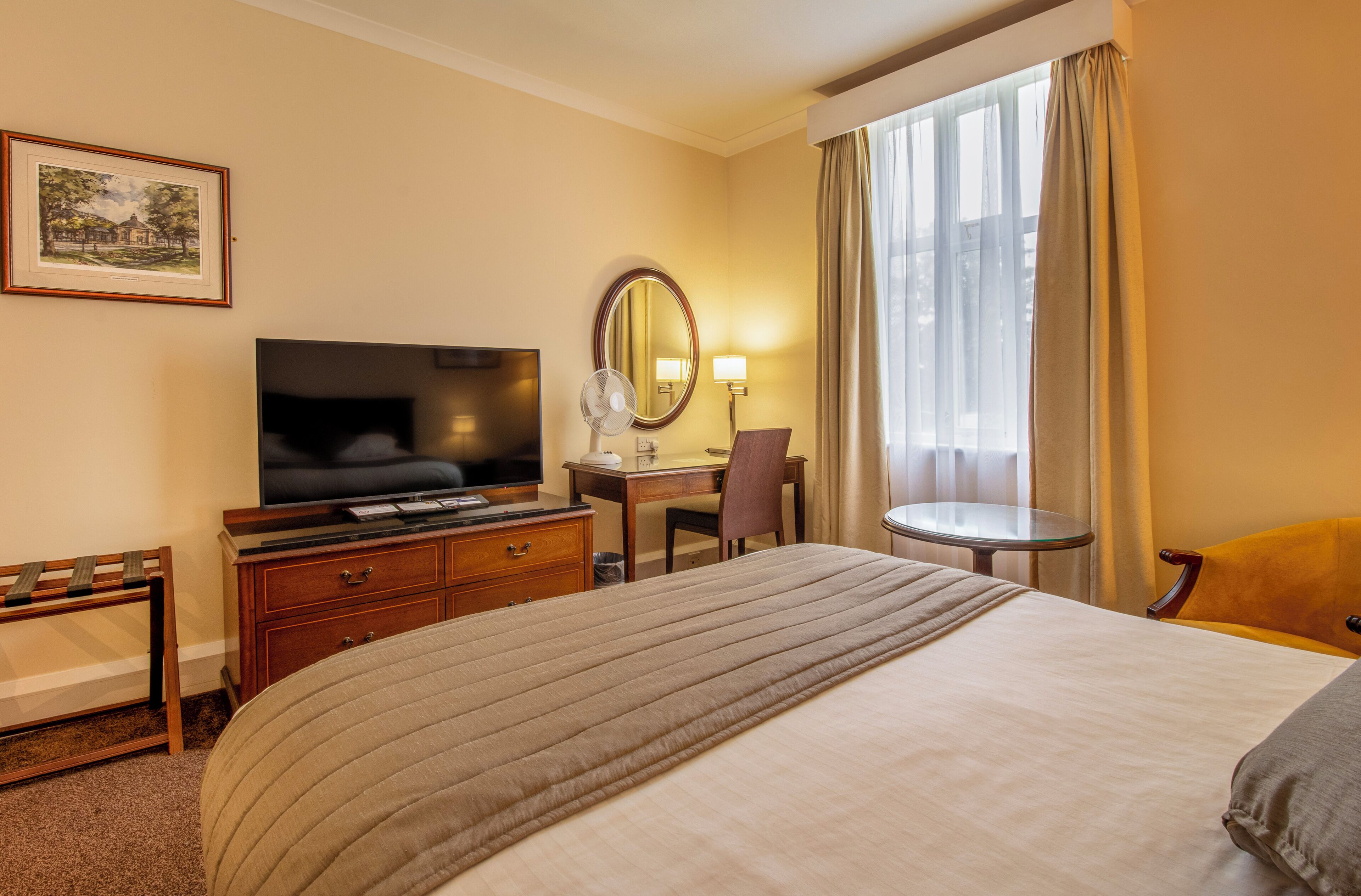 A hotel room with a large bed, a desk with a chair, a television, and a window with curtains.