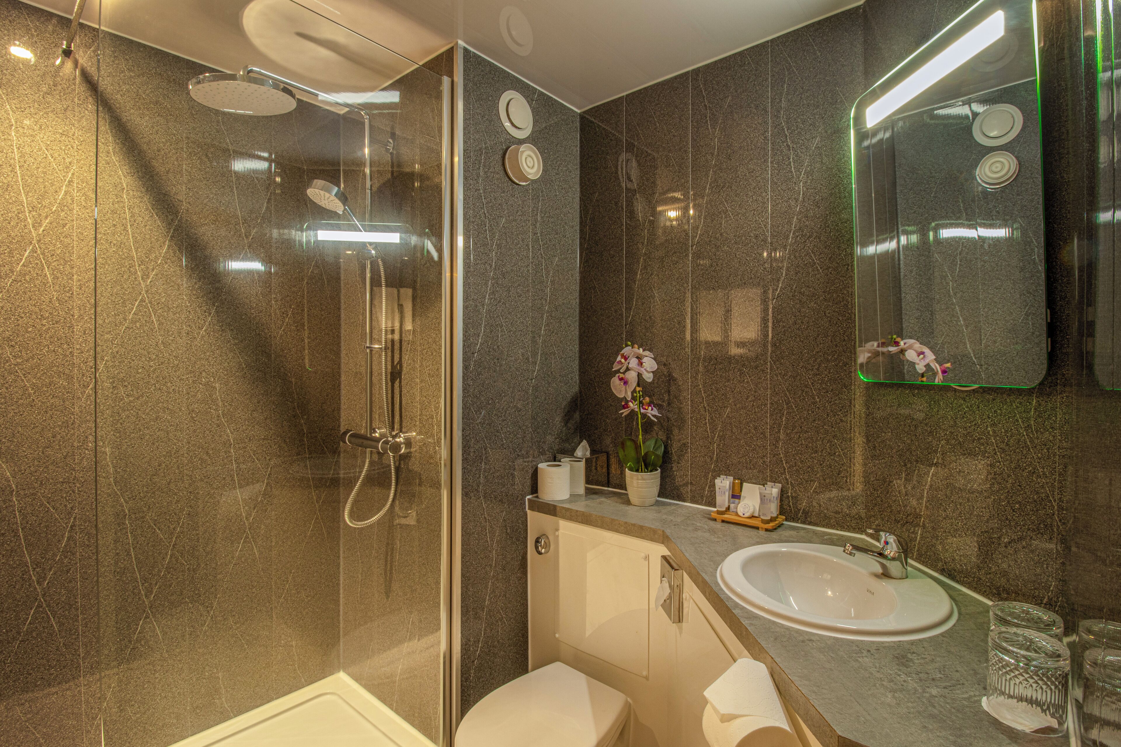 Un baño moderno con ducha envuelta en vidrio, un lavabo blanco y una pared con azulejos de mármol.